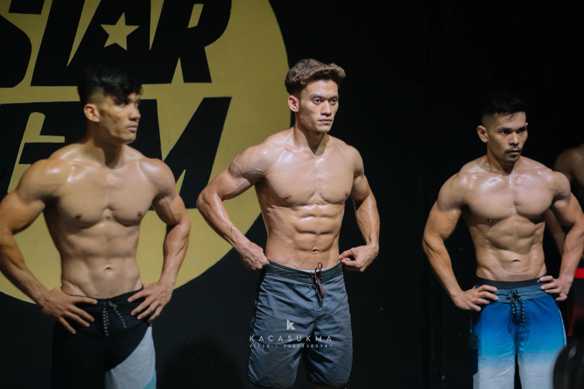 Three athletes posing side by side on stage under stage lighting